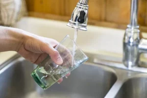 una persona riempie un bicchiere d'acqua trasparente al rubinetto della cucina