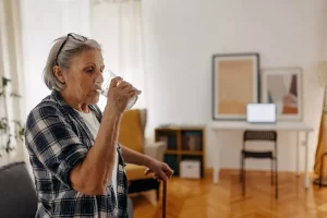 una donna anziana beve un bicchiere d'acqua nel salotto della propria casa