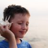 Bambino al mare con una conchiglia appoggiata all’orecchio: sentire bene è importante per la salute fisica e mentale