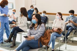 Persone con mascherina sedute in una sala d’attesa ambulatoriale, esempio di esposizione a virus e infezioni in ambienti affollati.