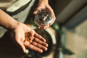 Mano che tiene capsule di integratori con bicchiere d’acqua, uso di supplementi per il dolore da endometriosi