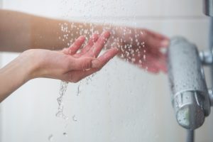 Mano sotto il getto della doccia per regolare acqua tiepida, consigli per evitare pelle secca e irritazioni da lavaggi frequenti
