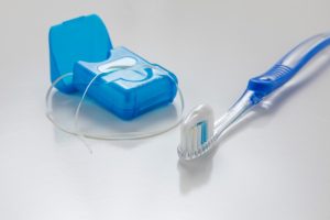 Spazzolino da denti e filo interdentale su superficie bianca, strumenti essenziali per l’igiene orale e la salute delle gengive.