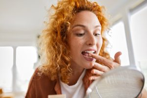 Donna che osserva i denti allo specchio per controllare la salute orale, utile per individuare segni di gengivite o parodontite.