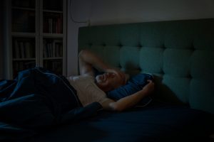 Persona sdraiata nel letto con difficoltà a dormire, insonnia e disturbi del sonno notturno