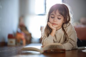 Bambina che legge un libro con concentrazione, simbolo dello sviluppo cognitivo e dell’importanza della lettura fin dall’infanzia.