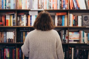 Persona davanti a una grande libreria mentre sceglie un libro, rappresentazione delle abitudini culturali e della stimolazione cognitiva.
