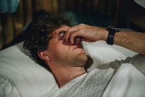 Uomo a letto con espressione di stanchezza e dolore, immagine legata ai sintomi neurologici e al malessere post-sforzo della ME/CFS.