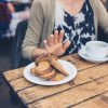Donna che rifiuta un piatto con pane e biscotti durante un pasto, gesto associato a una dieta senza glutine.