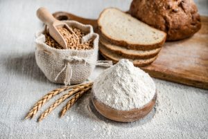 Farina di frumento, chicchi di cereali e pane su tavolo in legno, alimenti che contengono glutine comunemente presenti nella dieta.