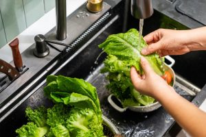 Persona che lava foglie di lattuga sotto acqua corrente in cucina prima della preparazione di un’insalata.