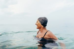 Donna anziana che nuota in mare aperto durante l'estate; esposizione solare e attività fisica favoriscono la produzione di vitamina D utile alla salute delle ossa