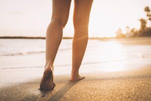 Persona che cammina sulla battigia al tramonto; l'attività fisica con carico del peso corporeo contribuisce al mantenimento della densità ossea