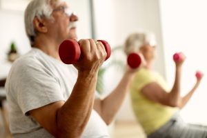 Uomini e donne anziani svolgono allenamento con pesi leggeri per mantenere massa muscolare, equilibrio e autonomia in età avanzata.