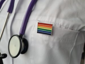 Camice medico con simbolo della bandiera LGBTQ+, rappresentazione dell’assistenza sanitaria inclusiva e del contrasto alle discriminazioni in ambito sanitario.