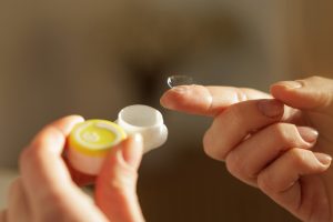 Mano che tiene una lente a contatto accanto al portalenti, simbolo della corretta gestione e conservazione delle lenti.