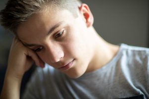 Primo piano di un ragazzo con espressione pensierosa e abbattuta, possibile manifestazione di sofferenza psicologica, isolamento emotivo o difficoltà nella gestione delle emozioni durante l’adolescenza.