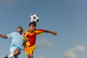 Due giovani calciatori contendono un pallone aereo con un colpo di testa durante una partita, gesto tecnico comune nel calcio giovanile.