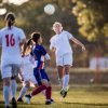 Partita di calcio femminile con una giocatrice che colpisce il pallone di testa durante un duello aereo.