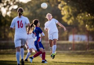 Partita di calcio femminile con una giocatrice che colpisce il pallone di testa durante un duello aereo.