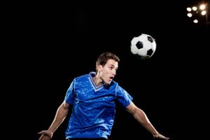 Calciatore esegue un colpo di testa durante una partita in notturna, immagine che rappresenta l'impatto tra testa e pallone studiato nelle ricerche neurologiche.
