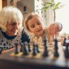 Una bambina e un'anziana condividono una partita a scacchi, esempio di attività intergenerazionale che mantiene attive attenzione e memoria.