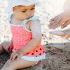 Adulto applica una crema solare SPF sulla pelle di una bambina seduta sulla sabbia, per proteggerla dai raggi UV durante una giornata al mare.