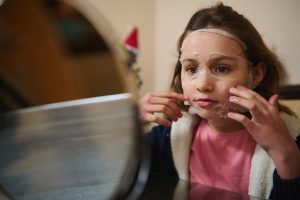 Bambina che applica una maschera cosmetica sul viso davanti allo specchio durante una routine di skincare.