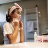 Bambina che applica un prodotto detergente sul viso in bagno durante la cura quotidiana della pelle.