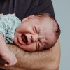 Adulto tiene in braccio un neonato che piange inconsolabilmente, situazione tipica della sindrome da distress infantile descritta dalle nuove linee guida.