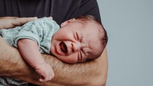 Adulto tiene in braccio un neonato che piange inconsolabilmente, situazione tipica della sindrome da distress infantile descritta dalle nuove linee guida.