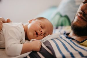 Neonato addormentato sul petto del padre durante il contatto pelle a pelle, pratica che favorisce conforto e regolazione del neonato.