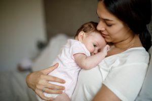 Madre tiene in braccio un neonato appoggiato alla spalla, una posizione che può aiutare a calmare il pianto e rassicurare il bambino.