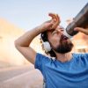 Persona che beve acqua durante una corsa estiva, con evidente sudorazione, per mantenere una corretta idratazione durante l'attività fisica.