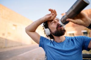Persona che beve acqua durante una corsa estiva, con evidente sudorazione, per mantenere una corretta idratazione durante l'attività fisica.