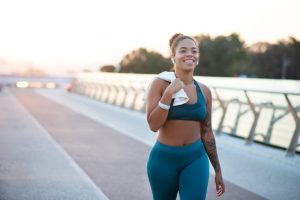 Donna in abbigliamento sportivo che cammina dopo l'allenamento con un asciugamano sulle spalle, esempio di recupero e reidratazione dopo l'esercizio.