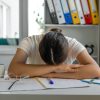 Persona stanca con la testa appoggiata sulla scrivania dopo il rientro dalle vacanze
