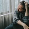 Uomo seduto vicino a una finestra con atteggiamento pensieroso e umore depresso, immagine che richiama i sintomi della depressione.