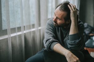 Uomo seduto vicino a una finestra con atteggiamento pensieroso e umore depresso, immagine che richiama i sintomi della depressione.