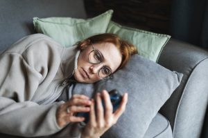 Persona sdraiata sul divano con espressione triste mentre osserva lo smartphone, immagine che rappresenta i sintomi della depressione e del disagio psicologico.