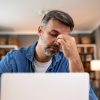 Uomo appare affaticato davanti al computer durante il lavoro da casa