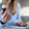 Donna mostra un flacone di medicinale mentre utilizza un computer, rappresentazione dell’acquisto di farmaci online