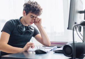 Adolescente con al collo delle cuffie, affaticato alla scrivania durante lo studio