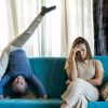 Donna adulta e vambina sul divano di casa. La donna sembra stressata, ha accanto la bambina che fa la verticale.