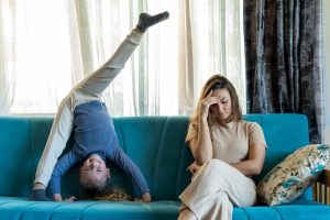 Donna adulta e vambina sul divano di casa. La donna sembra stressata, ha accanto la bambina che fa la verticale.