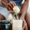 Persona versa una dose di proteine in polvere in uno shaker per preparare una bevanda integrativa.