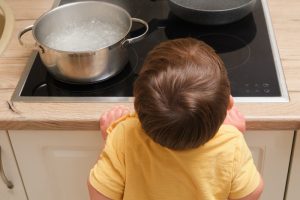 Bambino vicino a un piano cottura con una pentola in ebollizione, situazione che richiede attenzione per prevenire ustioni e incidenti in cucina